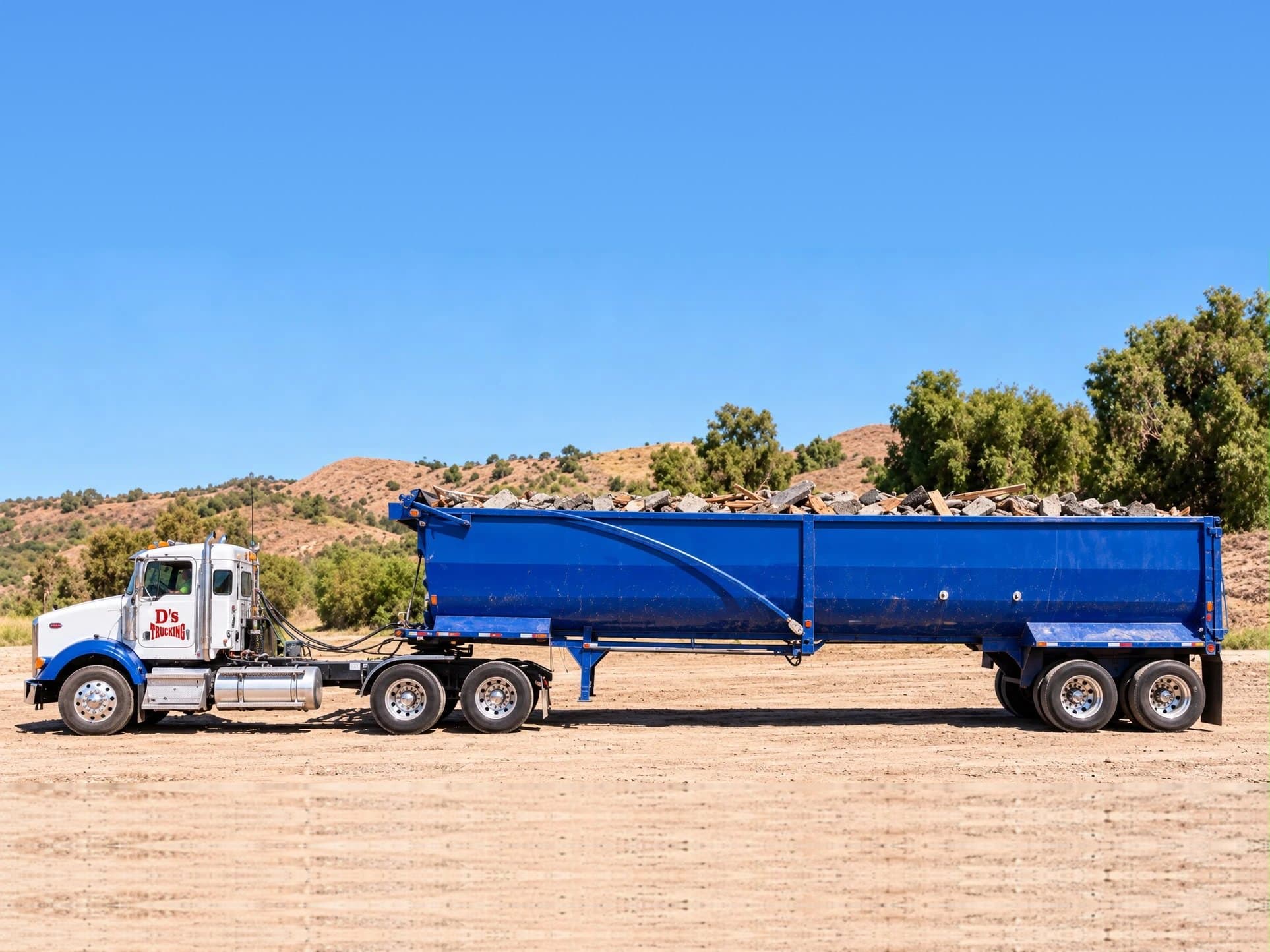 A D’s tractor pulling a blue high-side trailer loaded with broken concrete and lumber