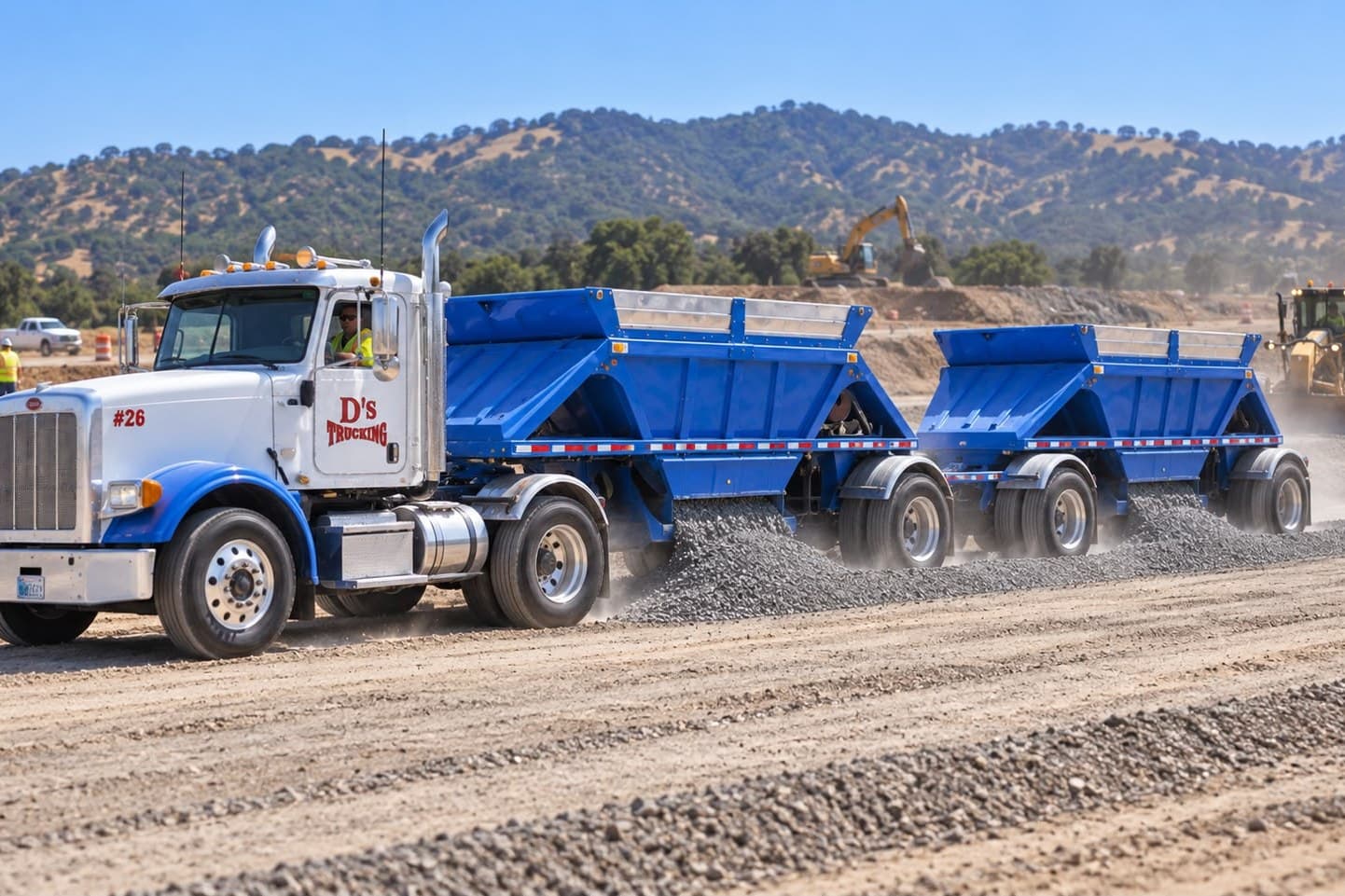 A D’s bottom-dump set laying base rock along a graded haul road